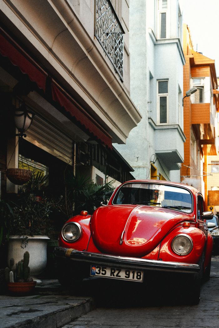A classic red Volkswagen Beetle parked on a narrow street in Istanbul, Türkiye.