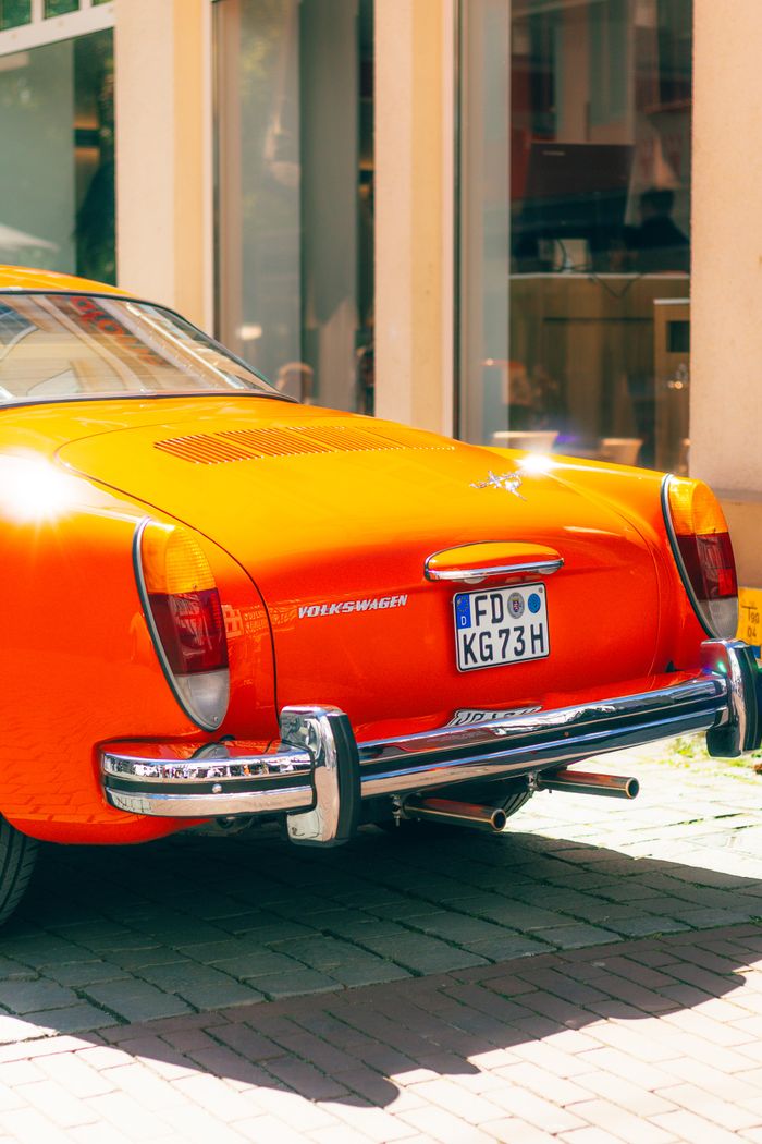 Rear view of a vibrant orange vintage Volkswagen car parked on a sunlit city street.