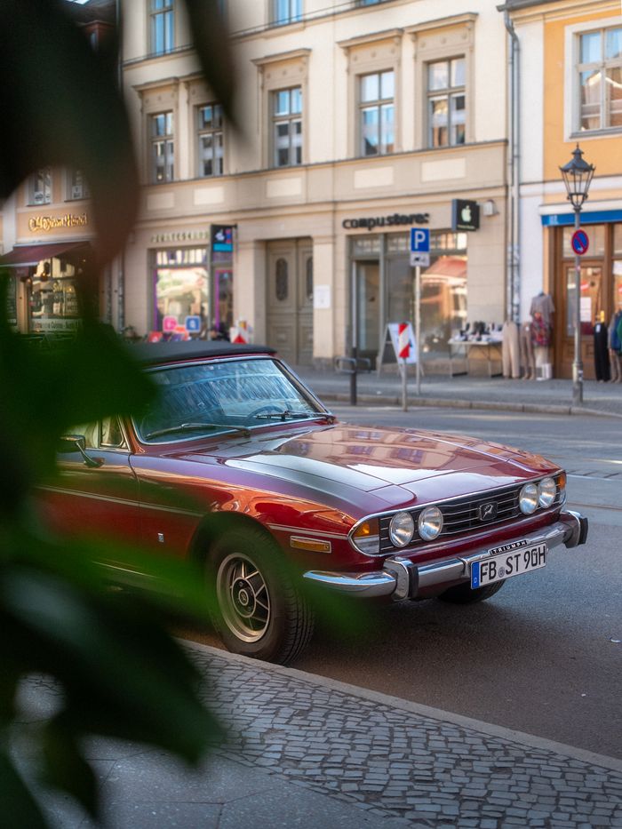 Classic red car parked on a cobblestone street in a European city, showcasing architectural charm.
